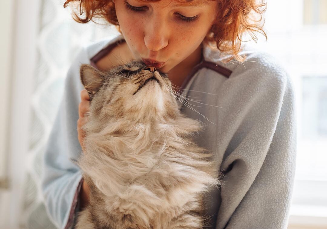 female with red curly hair kissing fluffy tabby cat indoors